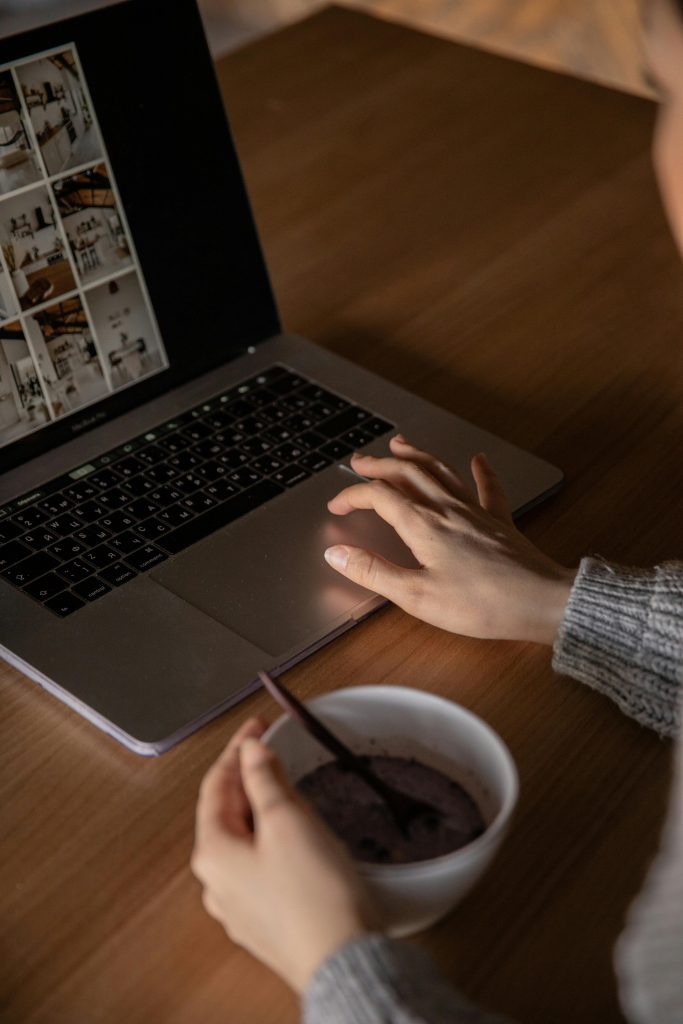 A person browsing stock photos on a laptop while enjoying a bowl of cereal at home.